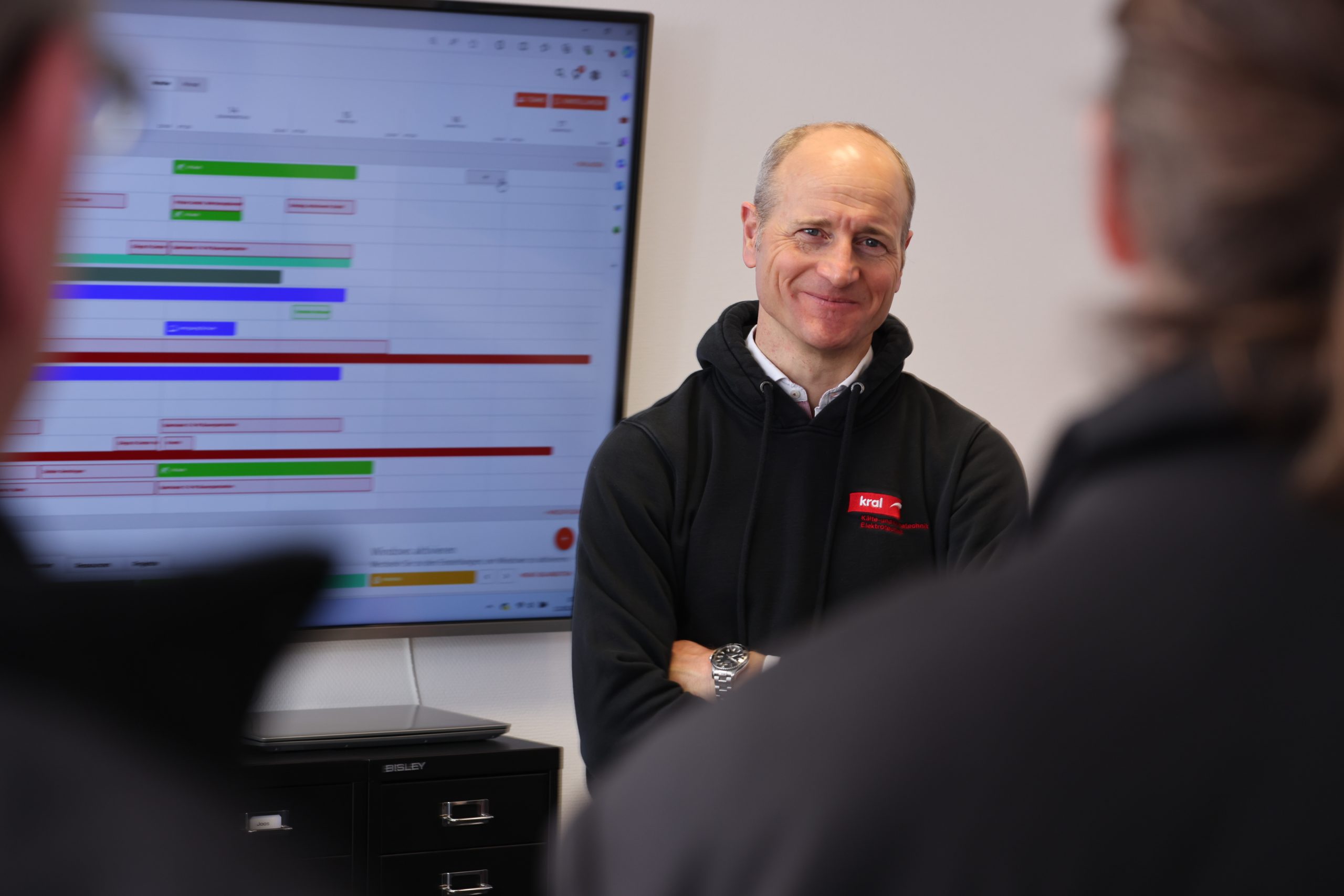 Ein junger Mann steht vor einer Gruppe mit verschränkten Armen und präsentiert etwas