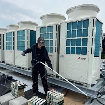 Ein junger Mann legt einen Kabelkanal an einem Verflüssiger auf dem Dach eines Gebäudes.